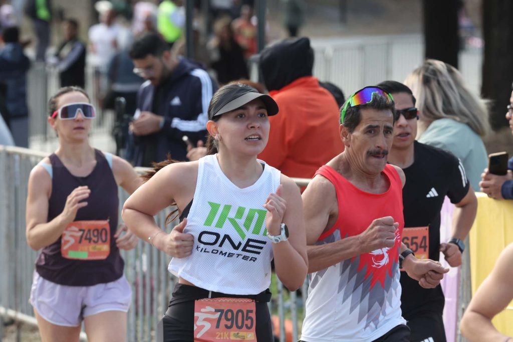 Corredores con nÃºmeros al pecho avanzan en una carrera de 21 kilÃ³metros junto a vallas y pÃºblico.