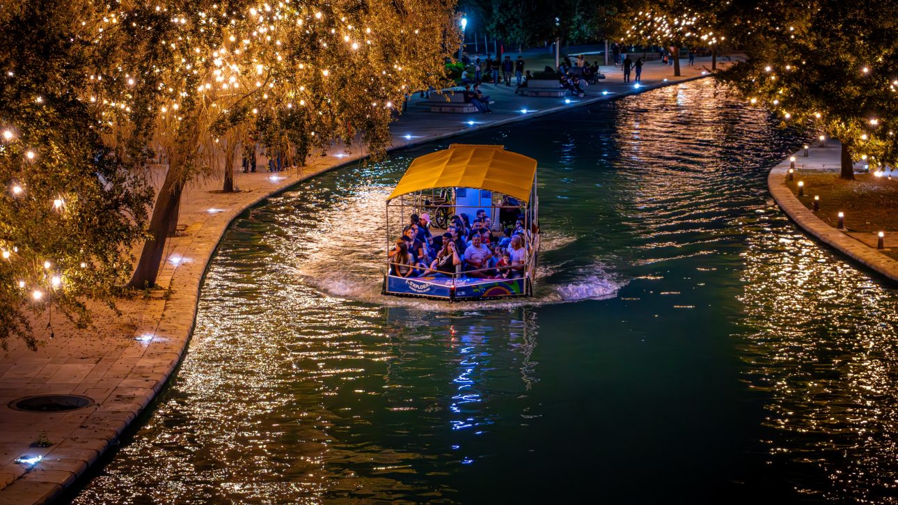Barco turÃ­stico navegando de noche por el canal entre Ã¡rboles cubiertos de luces cÃ¡lidas