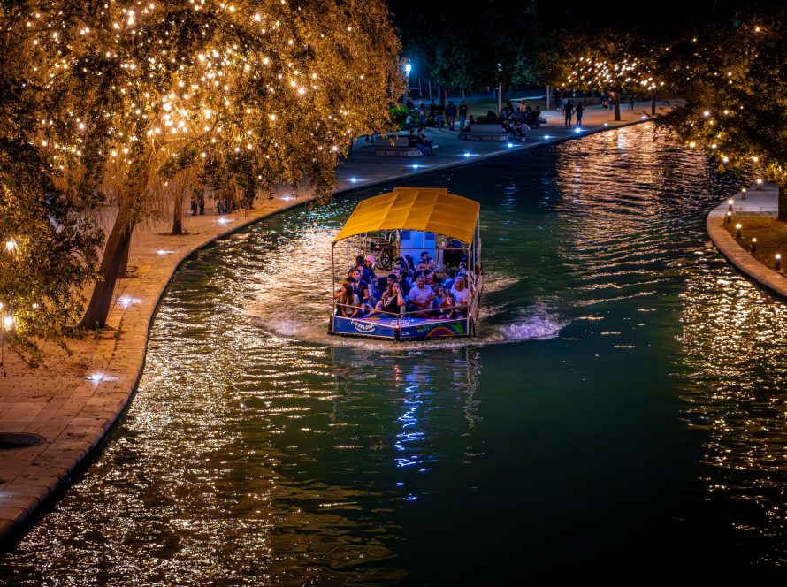 Barco turÃ­stico navegando de noche por el canal entre Ã¡rboles cubiertos de luces cÃ¡lidas