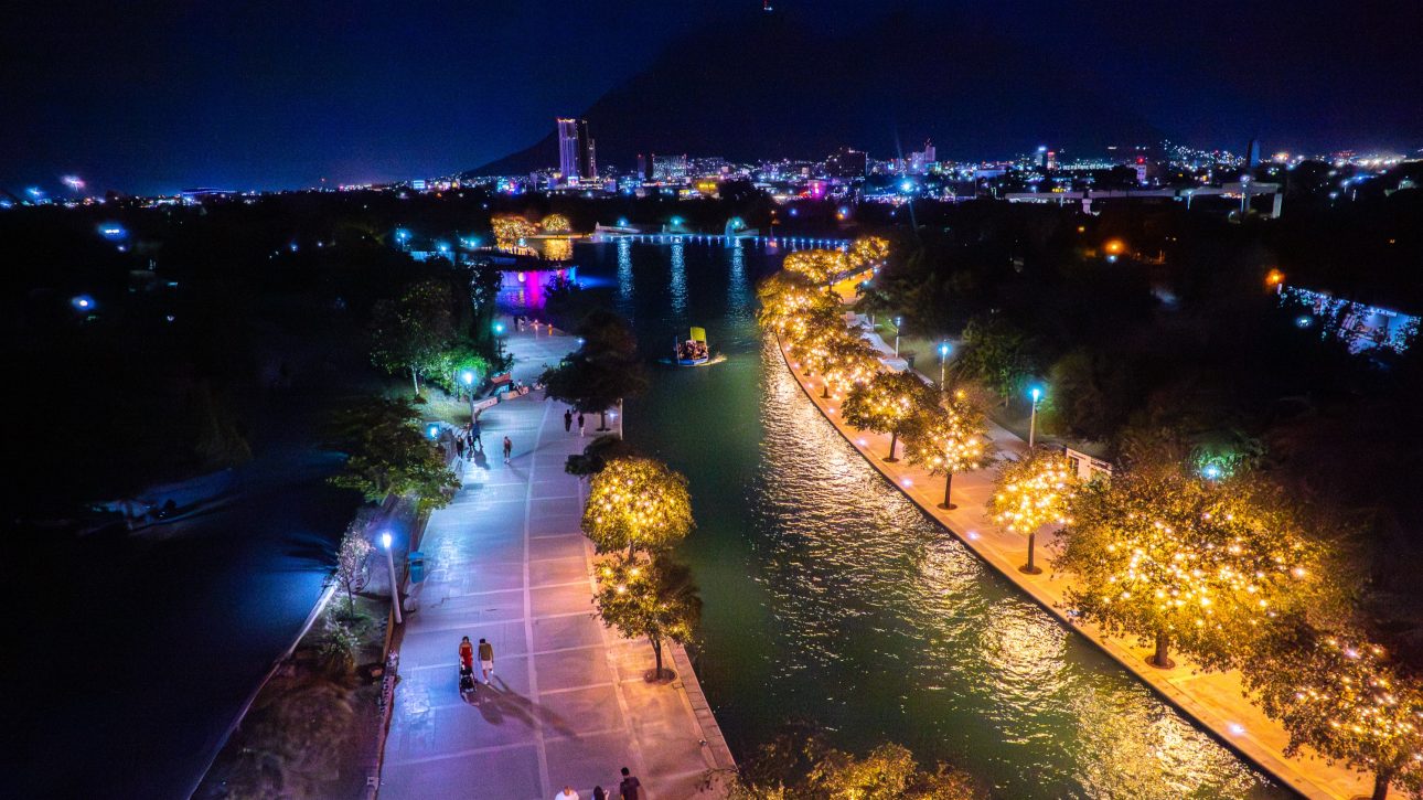Vista nocturna del canal del Paseo Santa LucÃ­a con barco turÃ­stico, Ã¡rboles iluminados y la ciudad al fondo.